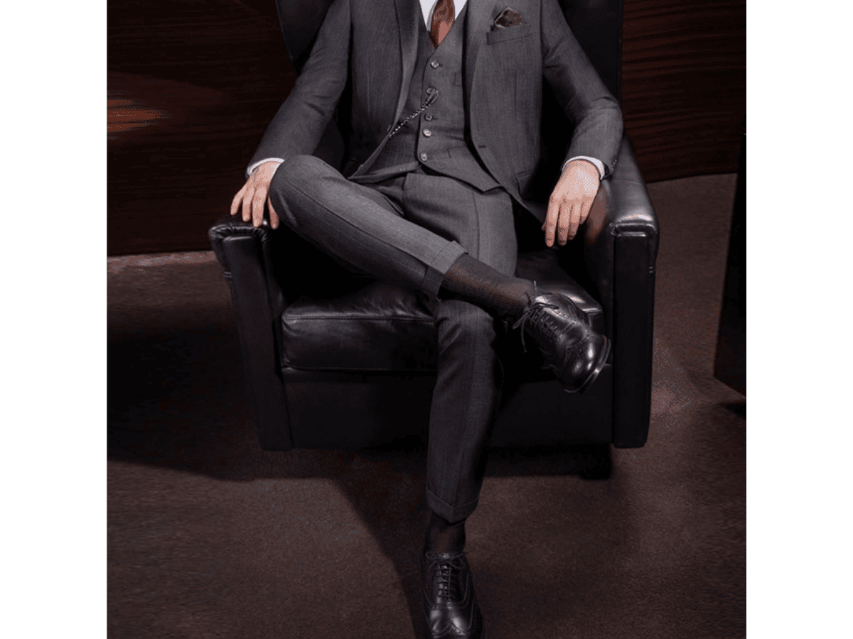 Người đàn ông mặc suit, ngồi bắt chéo chân, để lộ phần tất cổ cao tối màu, liền mạch và hài hòa với quần