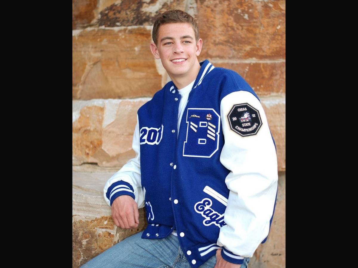 Người mẫu nam mặc áo khoác bóng chày, bên trong là áo thun trắng và quần jeans xanh