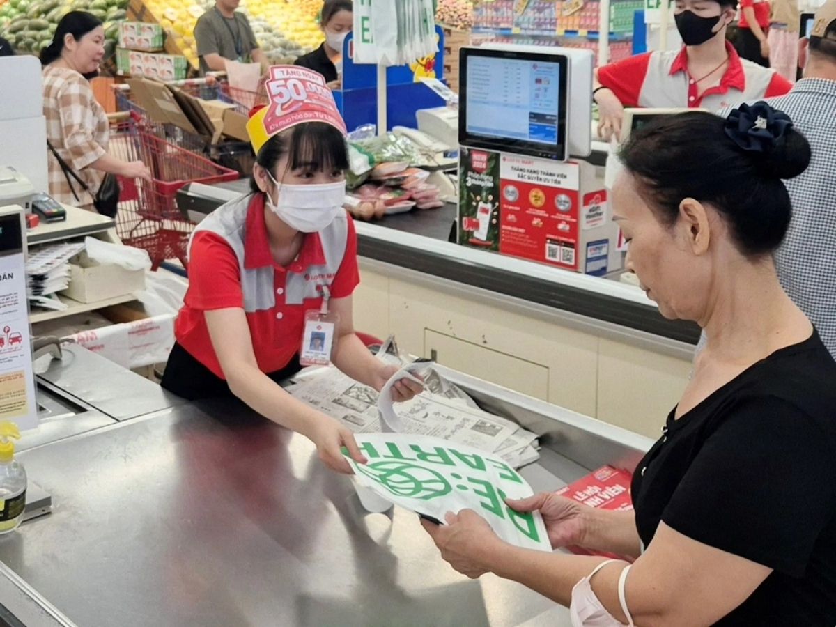 Nhân viên Lotte Mart mặc áo polo đỏ phối chi tiết xám, tươi cười hỗ trợ khách hàng trong siêu thị